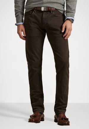 Braune Denim-Jeans mit glatter Textur, Fünf-Taschen-Design und einem braunen Ledergürtel. Kombiniert mit braunen Slippern und einem grauen Pullover.