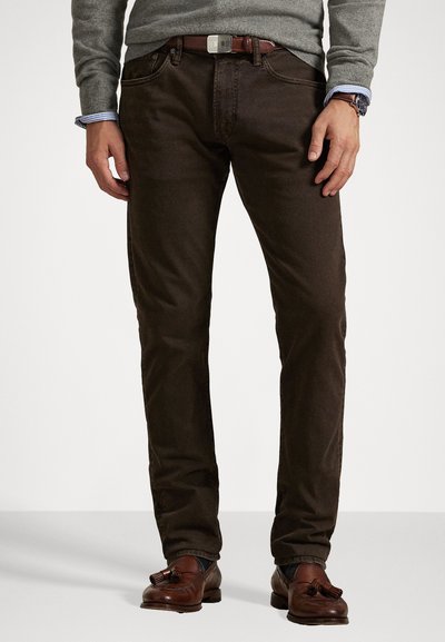 Bruine spijkerbroek van denim met een gladde textuur, vijf zakken en een bruine leren riem. Gepaard met bruine loafers en een grijze trui.