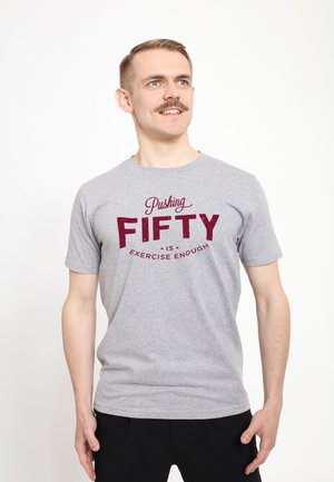 Šedé bavlněné tričko s tučným červeným nápisem "Pushing FIFTY is Exercise Enough." Krátké rukávy, kulatý výstřih, lehký materiál.