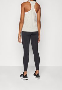 Top sin mangas de color beige claro con diseño de corte racer, combinado con leggings negros y zapatillas deportivas negras. Textura suave, detalles mínimos.