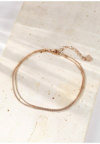 Braccialetto alla caviglia a doppio strato in oro rosa con catena a pallini e catena piatta, dotato di un piccolo ciondolo a forma di cuore e chiusura a moschettone.