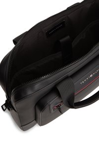 Μαύρη τσάντα χειρός Tommy Hilfiger με επάνω φερμουάρ, μπροστινή τσέπη, διπλές λαβές και επενδυμένο εσωτερικό διαμέρισμα για φορητό υπολογιστή.