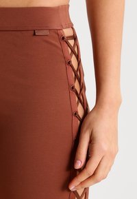 Falda marrón con cordones laterales y ojales metálicos. Confeccionada en una tela suave, tiene un diseño ajustado y una cintura alta.