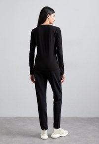 Top noir à manches longues avec un col rond, associé à un pantalon noir fuselé, présentant une texture lisse et des détails de couture subtils.