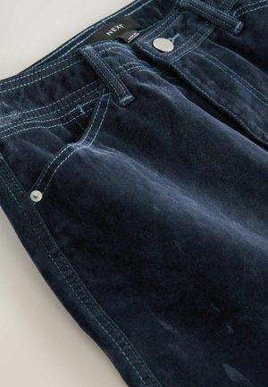 Marineblaue Cordhosen mit sichtbaren Nähten, Fronttaschen und Metallknopfverschluss. Weiche Textur, schräg verlaufende Taschennaht und sichtbares Markenlabel.