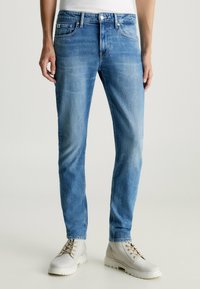 Jeans de mezclilla azul claro con un ajuste slim, que cuentan con cinco bolsillos, detalles de costura y cierre de cremallera. Combinados con botas de cordones gris claro.