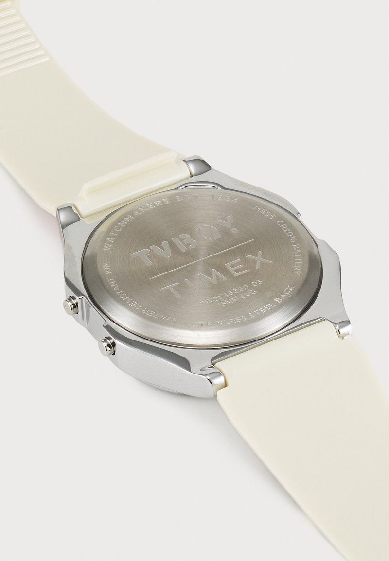 Reloj Timex con fondo de acero inoxidable, correa de silicona crema, dos botones laterales y detalles grabados en la parte posterior.