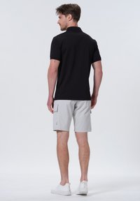 Sort kortærmet polo-skjorte, grå cargo-shorts med lommer og hvide sneakers. Minimalistisk design med en afslappet pasform og let tekstur.