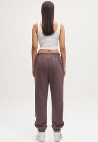 Witte katoenen crop top, gecombineerd met losse, lavendelkleurige joggers met een elastische tailleband en manchetten, gedragen met witte sneakers.