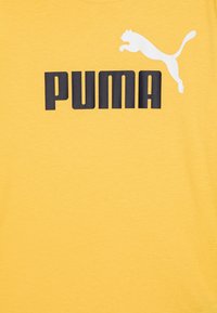 Camiseta de algodón amarilla con un logo negro de "PUMA" y un gráfico de un puma saltando en blanco, cuello redondo y mangas cortas. Textura ligera.
