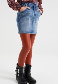 Denim mini suknja s izblijeđenim plavim pranjem, uparen s smeškim umetnim kožnim tajicama i crnim čizmama do gležnja s kopčama.