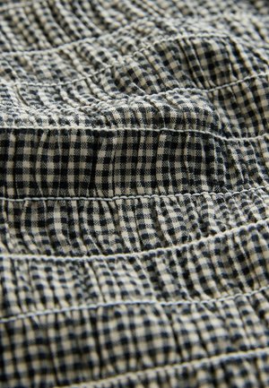 Mėlynos ir baltos gingamo audinys su susitraukiančia tekstūra, kurioje matomos horizontalaus siūlės ir minkšta, austinė išvaizda.