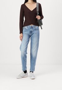 Brun omlottskjorta, ljusblå jeans med raka ben och grå sneakers med vita detaljer. Toppen har en djup V-ringning, långa ärmar och mjuk textur.