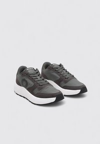 Zapatillas deportivas grises con parte superior de malla y material sintético, entresuela blanca, suela de goma negra y detalle de logo en el lateral.