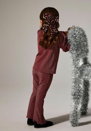 Bordeaux glitterend loungewear set met lange mouwen en broeken. Haar is strak teruggebonden met een grote paillettenstrik. Houdt een zilveren glinsterdecoratie vast.