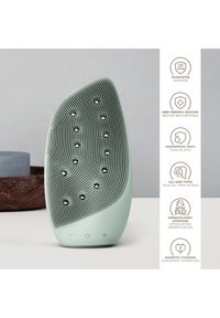 Grön silikon ansiktsrengöringsenhet med texturerad yta, rundad form och vattentålig design; har knappar för användning.