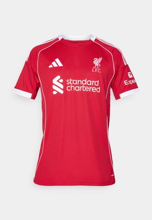 Maillot de football rouge à manches courtes en polyester, avec des accents blancs, un col rond et des logos pour L.F.C. et Standard Chartered.