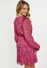 Rosa Leopardenmuster-Kleid mit Rüschensäulen, tailliertem Bund und gestuftem Rock. Durchsichtiger Stoff mit zarten Akzenten und einer fließenden Silhouette.