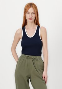 Mørkeblå ærmeløs tanktop med hvid kant, parret med løse olivengrønne bukser, der har elastisk talje og sidelommer.
