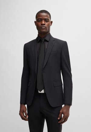 Schwarzer maßgeschneiderter Anzug mit schlanker Passform, bestehend aus einem einreihigen Blazer mit Reverskragen, kombiniert mit einer passenden schwarzen Krawatte und einem Hemd.