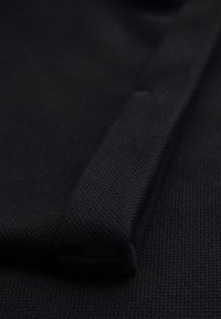 Close-up of black textured fabric with a folded edge detail on a flat surface.