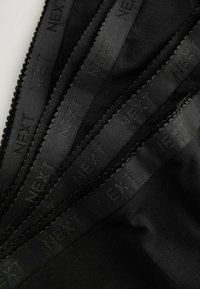 Tessuto nero con cinque nastri etichettati "NEXT" e un bordo a ondulato. Texture liscia, che mostra un aspetto elegante e uniforme.