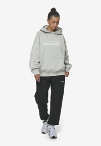 Gray oversized hoodie with "PEGADOR" logo, kangaroo pocket, and white accents, paired with black loose-fit pants and white sneakers.