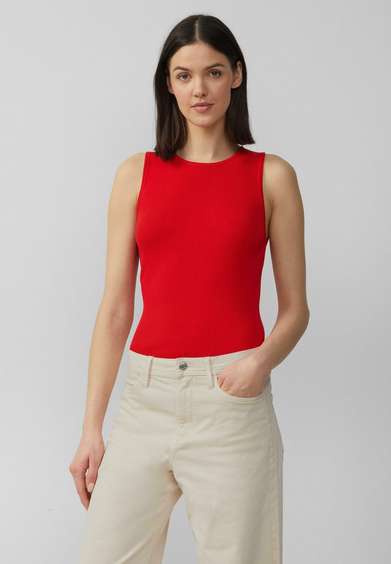 Rotes geripptes ärmelloses Oberteil, kombiniert mit beigen High-Waist-Hosen, mit Rundhalsausschnitt und subtiler Textur.