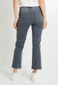 Vaqueros de campana grises con bolsillos traseros, que presentan una textura suave y una cintura de altura media, combinados con zapatillas blancas.