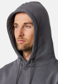 Felpa grigia con cappuccio regolabile, texture liscia e vestibilità rilassata. Presenta dettagli di cucitura sottili attorno al collo e al cappuccio.