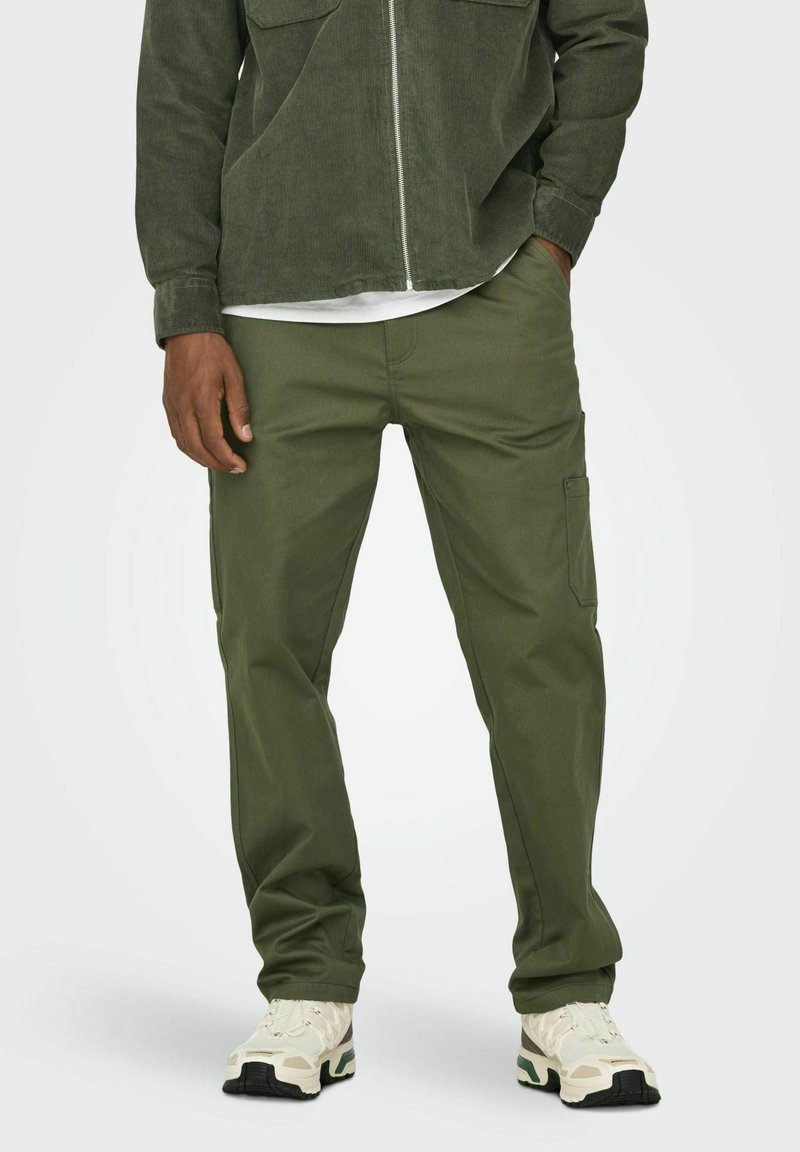 Pantalones cargo verde oliva hechos de una tela texturizada, con un corte ajustado y bolsillos laterales, combinados con zapatillas de color claro.