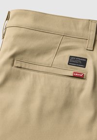 Beežist puuvillasegustest püksid, millel on tagatasku ja Levi'si brändi silt. Kangas on sileda tekstuuriga ja klassikalise, kohandatud disainiga.