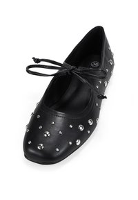 Zapato plano de cuero negro con tachuelas plateadas, punta cuadrada y una correa con lazo atado en la parte superior, talla 36 en el interior.