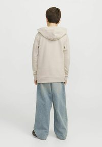 Felpa beige con cappuccio regolabile, abbinata a jeans a gamba larga blu chiaro. Materiale in cotone morbido con polsini e orlo a coste.