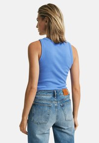 Helles blaues ärmelloses Top aus weichem Baumwollstoff, kombiniert mit hellblauen hochgeschnittenen Jeans mit Gesäßtaschen und einem Lederlabel.