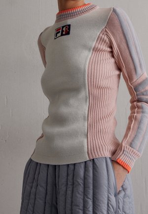 Pull en tricot ajusté avec devant crème, côtés et manches côtelés roses, poignet orange, et petit logo bleu et rouge sur la poitrine.