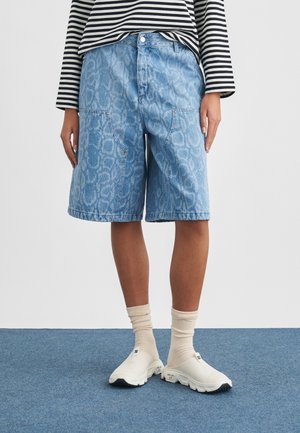 Pantaloncini di jeans azzurri con un motivo sottile, dotati di tasche anteriori e vestibilità comoda. Abbinati a scarpe bianche slip-on e calzini chiari.