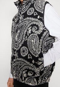 Gilet in pile con motivo paisley in bianco e nero, colletto alto e zip frontale; presenta un materiale testurizzato e soffice.