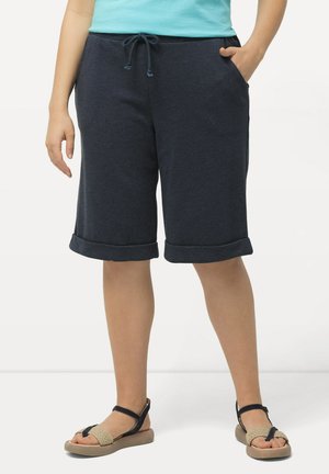 Granatowe szorty z bawełnianej mieszanki z wiązanym pasem, bocznymi kieszeniami i podwiniętymi mankietami, w zestawie z jasnymi sandałami.
