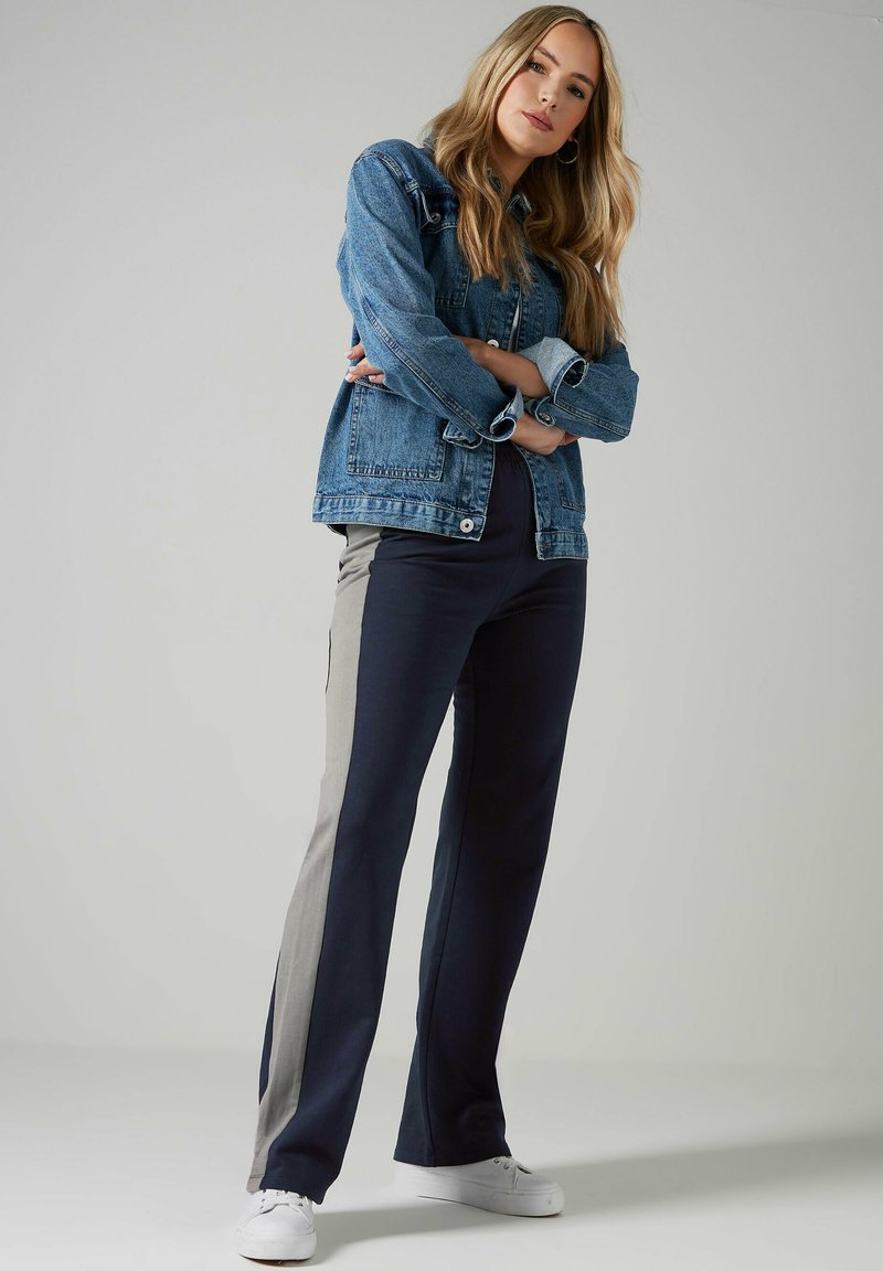 Jeansjack met twee borstzakken; grijs en marineblauwe kleurgebroken broek met zijzakken; witte sneakers; gladde textuur.