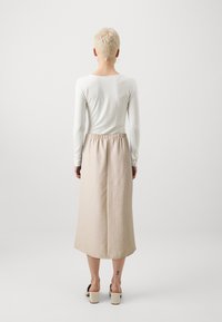 Jupe longue beige avec ceinture élastique, associée à une chemise blanche à manches longues. Tissu lisse, longueur sous le genou, conception simple.