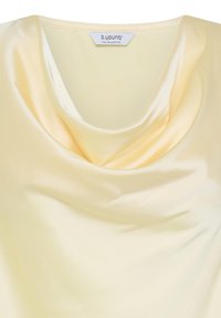 Haut en satin jaune pâle avec un col bénitier drapé et une étiquette de marque visible au niveau du col arrière.