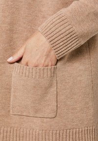 Lichtbruin gebreid sweatshirt met een geribde manchette en een voorkant met een ribbelrand, dat een zachte textuur en een casual ontwerp heeft.