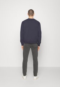 Mörkblå sweatshirt med rund halsringning, ribbade muddar och nederkant; kombinerad med mörkgrå jeans och vita joggingskor, sedd bakifrån.
