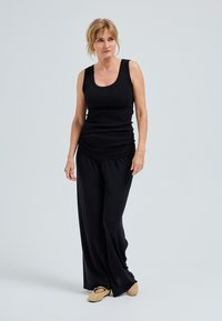 Zwarte mouwloze top van zachte stof, gecombineerd met losse zwarte broeken en beige instapschoenen. Eenvoudig ontwerp, relaxte pasvorm.