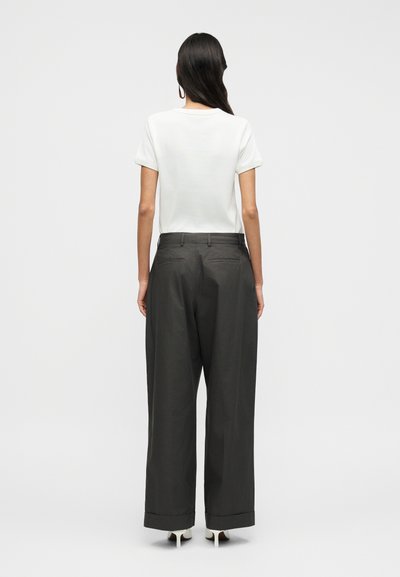 Λευκό κοντομάνικο T-shirt σε συνδυασμό με σκούρο, φαρδύ παντελόνι με διπλωμένο στρίφωμα και πίσω τσέπες, σε απλό φόντο.