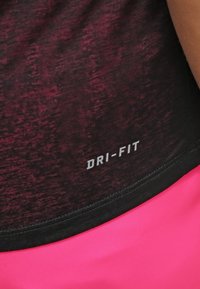 Punainen ja musta Dri-FIT urheilupaita teksturoidulla kankaalla, pyöristetyllä helmalla ja valkoisella painetulla logolla alareunassa.