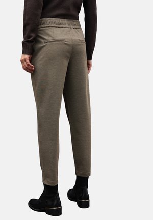Khaki schmal zulaufende Hose mit strukturiertem Finish, elastischem Bund und zwei mit Reißverschluss versehenen Gesäßtaschen, kombiniert mit schwarzen Stiefeletten.