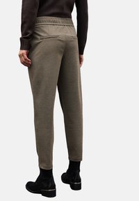 Khaki tapered broek met een gestructureerde afwerking, elastische tailleband en twee met rits afgesloten achterzakken, gecombineerd met zwarte enkellaarzen.
