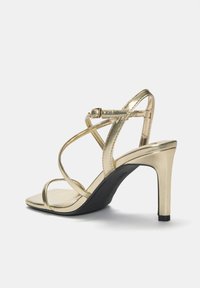 Zlaté sandály na vysokém podpatku s elegantním metalickým povrchem, otevřenou špičkou, štíhlými pásky a tvarovanou černou podešví.